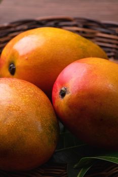 Mango. Close up of fresh ripe mango fruit on a bamboo sieve over dark wooden table background with green leaves.