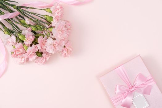 Mother's day background concept. Top view design of holiday greeting gift with carnation bouquet on bright pink table background