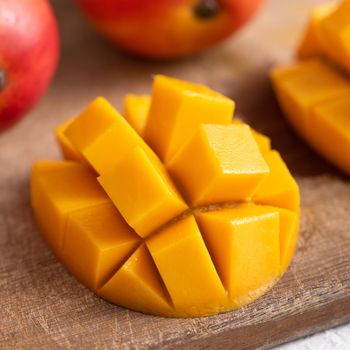 Diced fresh mango fruit on wooden cutting board with sunlight and leaf shadow at home kitchen in the afternoon.