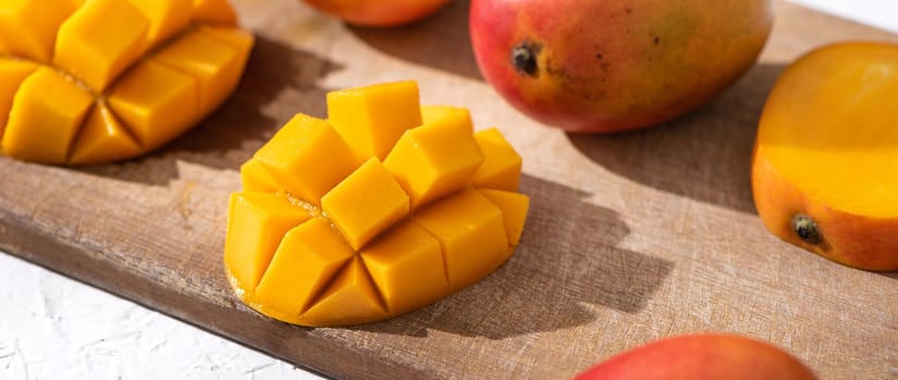 Diced fresh mango fruit on wooden cutting board with sunlight and leaf shadow at home kitchen in the afternoon.