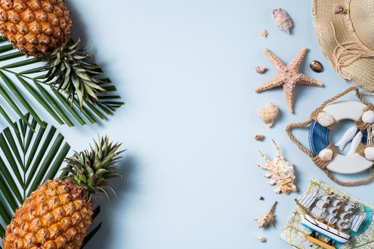 Summer fruit background design concept. Top view of holiday travel beach with shells, hat, pineapple and palm leaves on blue background.