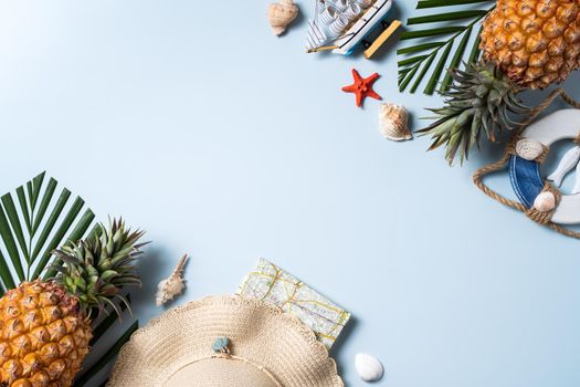 Summer fruit background design concept. Top view of holiday travel beach with shells, hat, pineapple and palm leaves on blue background.