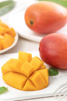 Diced fresh mango fruit on a white plate with leaves over wooden table background.