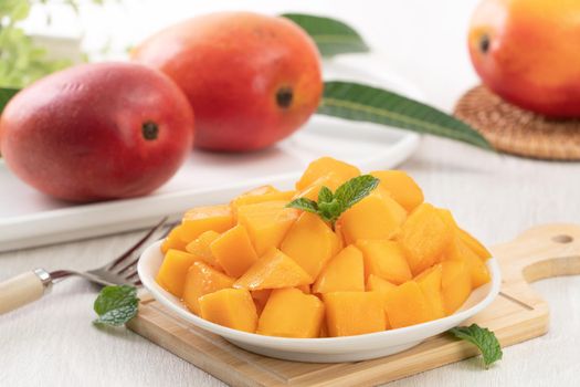 Diced fresh mango fruit on a white plate with leaves over wooden table background.