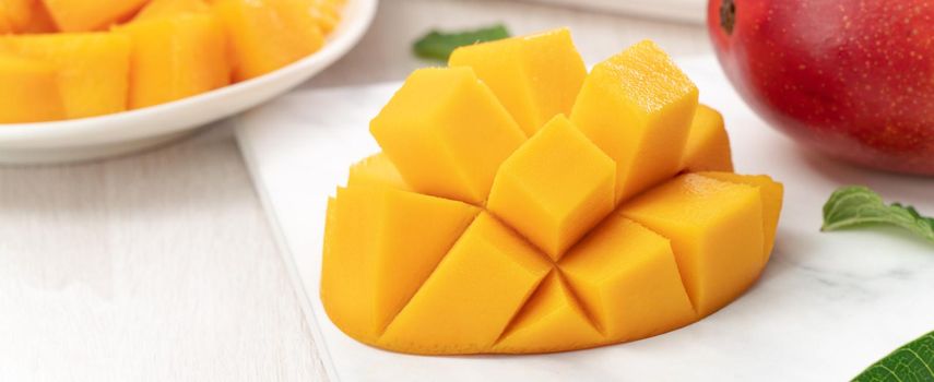 Diced fresh mango fruit on a white plate with leaves over wooden table background.