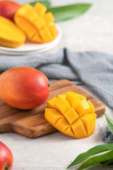 Diced fresh mango fruit on a white plate over wooden cutting board with leaves on gray table background.