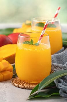Fresh beautiful delicious mango juice. Close up design concept of smoothie cold drink in a glass cup with paper straw on gray table background.