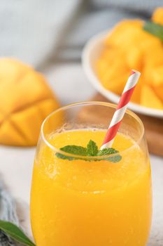 Fresh beautiful delicious mango juice. Close up design concept of smoothie cold drink in a glass cup with paper straw on gray table background.