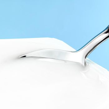 Yogurt cup and silver spoon on blue background, white plastic container, fresh dairy product for healthy diet and nutrition.