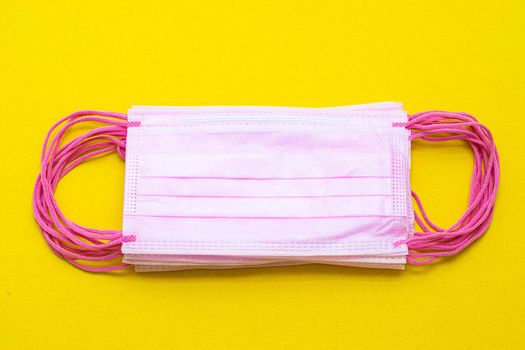 Medical mask isolated on a yellow background . Pink face mask. Article about the second wave of coronavirus. Protection of the respiratory system. Pneumonia and coronavirus. Pandemic. Copy space