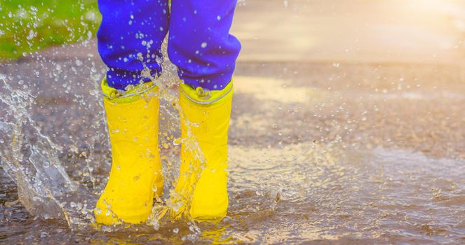 My rubber-booted feet are Bouncing in a puddle. Article about rubber boots. Children's summer shoes. Puddles after rain. Bad weather. A child jumps in a puddle. A happy boy in rubber boots jumps in puddles.