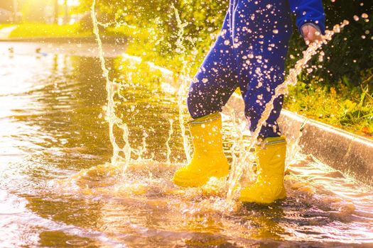 My rubber-booted feet are Bouncing in a puddle. Article about rubber boots. Children's summer shoes. Puddles after rain. Bad weather. A child jumps in a puddle. A happy boy in rubber boots jumps in puddles.