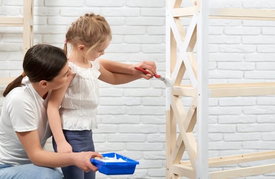 Close up of young mother and child painting wooden rack at home. Concept of family time.