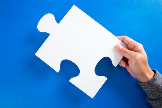 hands holding big paper white blank puzzles on a blue background, concept of business