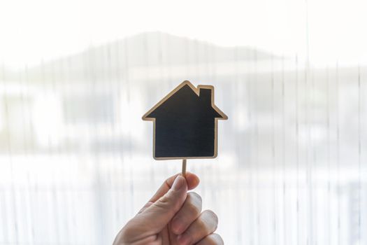 Real estate agent holding house shaped wood(Space for text input) on Blurred house background.