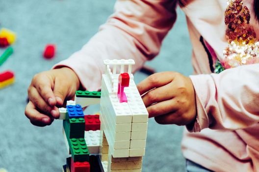 Little girl playing with colorful bricks at home or kindergarten. Closeup