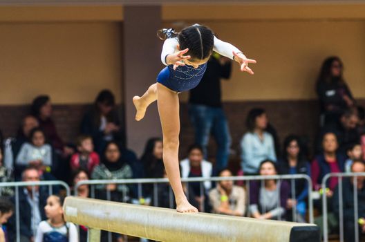 Young female gymnast performing handstand on balance beam, side view