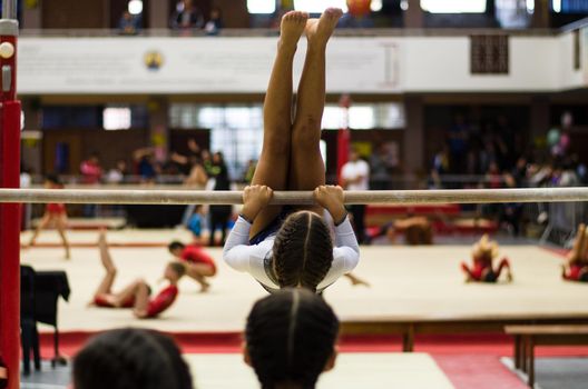 Athletic little girl gymnast performing exercises at the bar in the championship