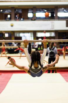 Athletic little girl gymnast performing exercises at the bar in the championship