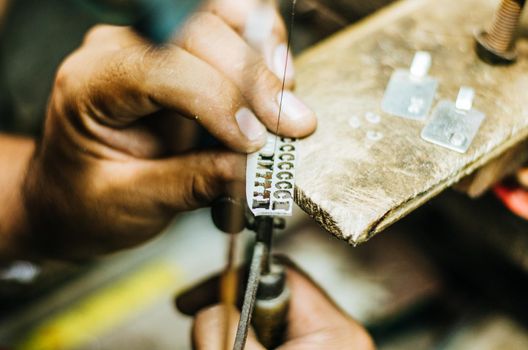 man's hands goldsmith work on a piece of silver with a metal saw on the work table, close up, selected focus, narrow depth of field