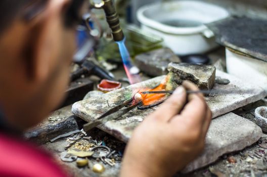 Master jeweler welding an ornament in a jewelry workshop. Image of hands and product close up.