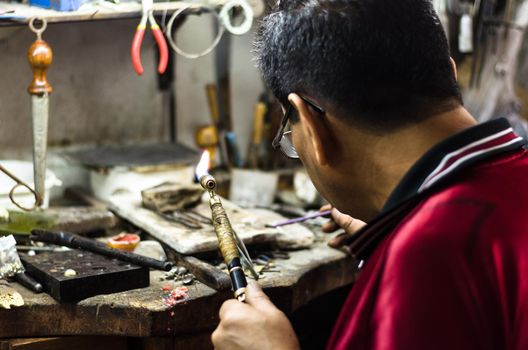 Master jeweler welding an ornament in a jewelry workshop. Image of hands and product close up.