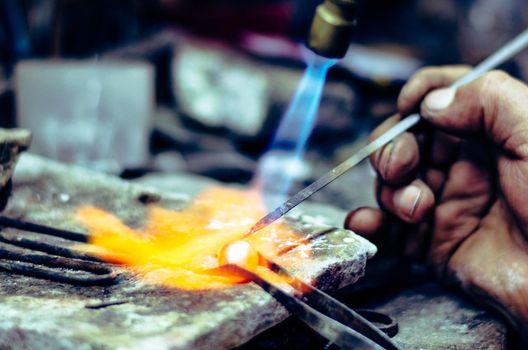 Master jeweler welding an ornament in a jewelry workshop. Image of hands and product close up.