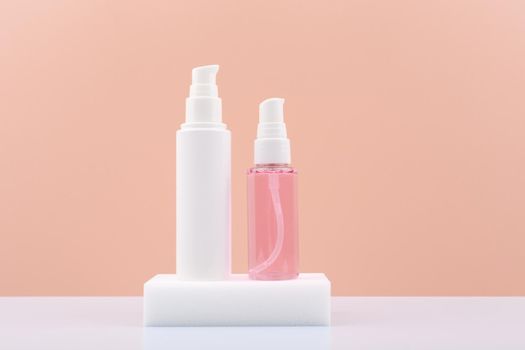 Cosmetic tubes with face cream and pink gel or foam for skin cleaning or exfoliating on white pedestal against pink background with copy space