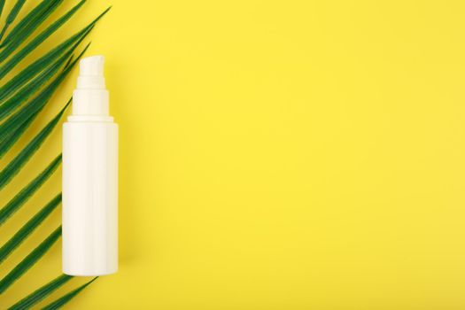 Face cream with sunblock in white tube against yellow background with palm leaf and copy space. Concept of sunblock and cosmetic beauty products with UV protection