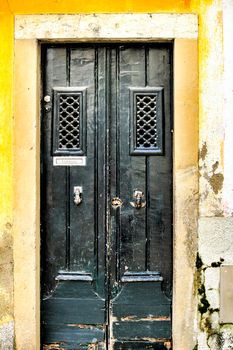 Old and colorful wooden door with door knocker hand shape in Lisbon, Portugal. Post word in portuguese written on it.