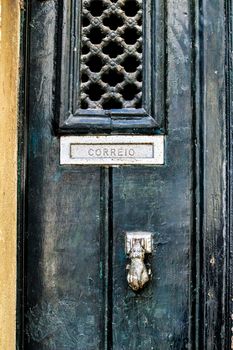 Old and colorful wooden door with door knocker hand shape in Lisbon, Portugal. Post word in portuguese written on it.