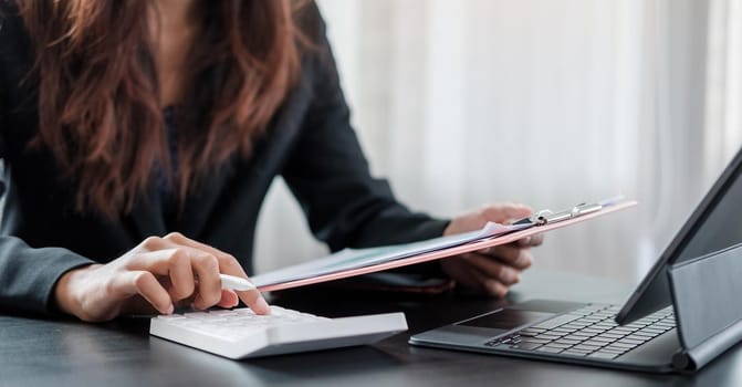 Woman with financial report and calculator. Woman using calculator to calculate report at the table in office.