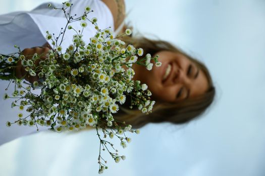 portrait of a happy flirty beautiful blonde woman in white blouse in the field. Carrying a bouquet of daisies. Temporary tattoo. Drawings on body. hippie. Nature loving.