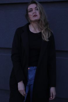 urban portrait of a pensive flirty cool beautiful woman in black blouse and jeans on a background of gray wall in strips