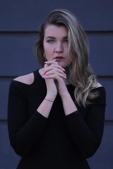 urban portrait of a pensive flirty beautiful young woman in black blouse on a background of gray wall in strips