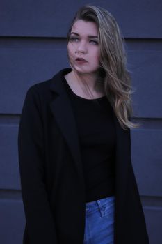 urban portrait of a pensive flirty cool beautiful woman in black blouse and jeans on a background of gray wall in strips