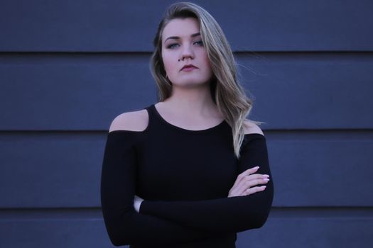 urban portrait of a pensive flirty beautiful young woman in black blouse on a background of gray wall in strips