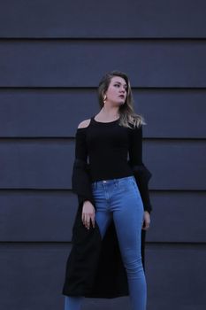 urban portrait of a pensive flirty cool beautiful woman in black blouse and jeans on a background of gray wall in strips