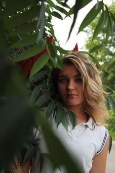 portrait of a flirty beautiful woman in white sport dress holding a tree branch in the tropical forest. Luxury resort.