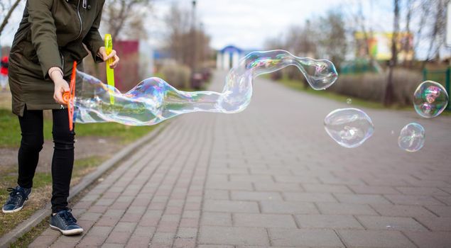 A girl blows soap bubbles in the park for the entertainment of children. Large, colorful soap bubbles in the open air in a public park.