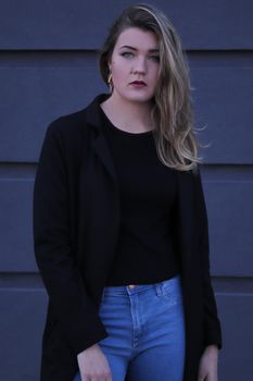 urban portrait of a pensive flirty cool beautiful woman in black blouse and jeans on a background of gray wall in strips