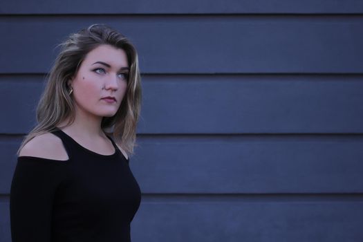 urban portrait of a pensive flirty beautiful young woman in black blouse on a background of gray wall in strips