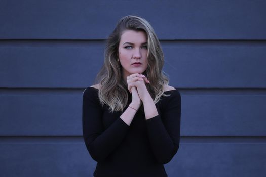 urban portrait of a pensive flirty beautiful young woman in black blouse on a background of gray wall in strips