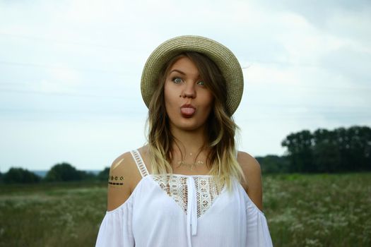 portrait of a happy flirty beautiful blonde woman in white blouse and straw hat in the field. Temporary tattoo. Drawings on body. hippie. Nature loving.