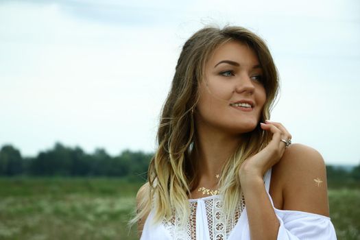 portrait of a happy flirty beautiful blonde woman in white blouse in the field. Temporary tattoo. Drawings on body. hippie. Nature loving.