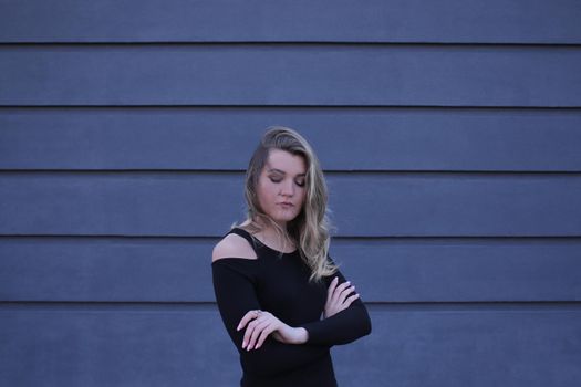 urban portrait of a pensive flirty beautiful young woman in black blouse on a background of gray wall in strips