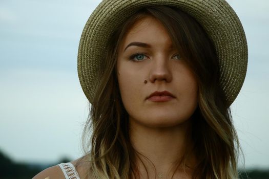 portrait of a pensive beautiful blonde woman in white blouse and straw hat in the field. Temporary tattoo. Drawings on body. hippie. Nature loving.