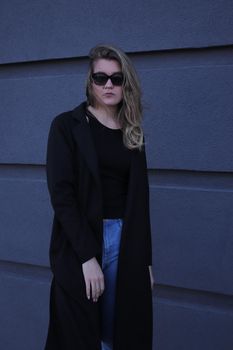 urban portrait of a pensive flirty cool beautiful woman in black blouse and jeans on a background of gray wall in strips