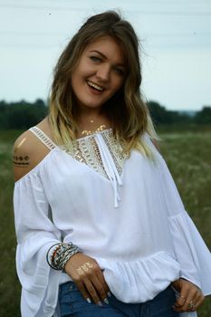 portrait of a happy flirty beautiful blonde woman in white blouse in the field. Temporary tattoo. Drawings on body. hippie. Nature loving.