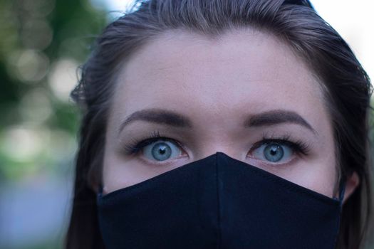 Pretty young blonde woman in medical black face mask. Wearing a t-shirt and jeans shorts. in a park. modern reality. covid-19 concept. copy space. High quality photo